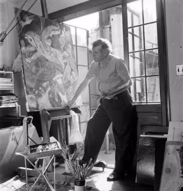 Marc Chagall with graying hair, leaning against the base of an easel holding the painting The Red Horse, earlier version.