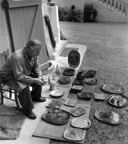 Marc Chagall, assis dans une cour intérieure, regarde une vingtaine de céramiques posées devant lui.