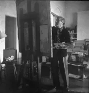 Marc Chagall with graying hair, color palette in hand, working on a large painting seen from behind.