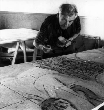 Chagall leaning on a square of the ceramic piece entitled The Crossing of the Red Sea, in which many characters are represented.