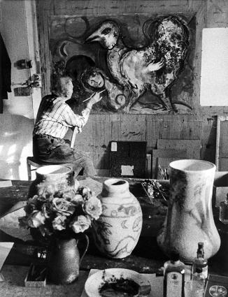 Chagall painting the female figure of a sketch entitled The Blue Rooster, with two painted vases in the foreground.