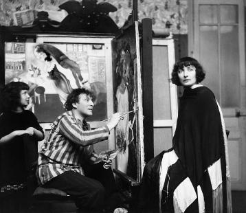 Bella pose pour Marc Chagall dans un salon, sous le regard de leur fille Ida, œuvre intitulée l'anniversaire en arrière-plan.