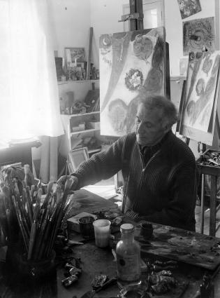Chagall with gray hair, working, sitting in front of the Eiffel Tower painting and its sketch.