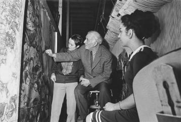 An elderly Marc Chagall, pointing out details of a wool tapestry to two young women working in the Gobelins workshop.