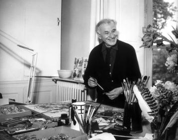 Chagall sourit parmi des pinceaux, des fleurs et des plumes rangées dans l'atelier.