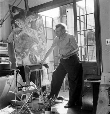 Marc Chagall with graying hair, leaning against the base of an easel holding the painting The Red Horse, earlier version.