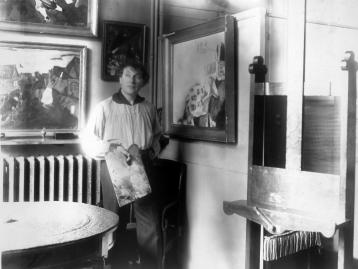 A young Marc Chagall, palette in hand, posing in front of four paintings: Birthday, Death, Birth, and The Dream.