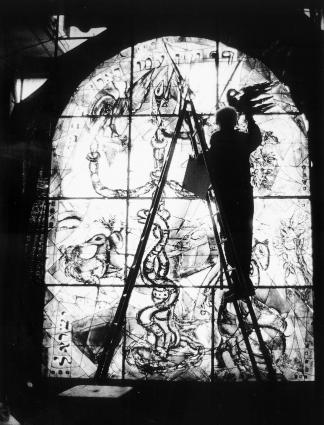 Chagall debout sur une échelle, travaillant  sur un détail (représentant un oiseau)  d'un vitrail pour une synagogue.