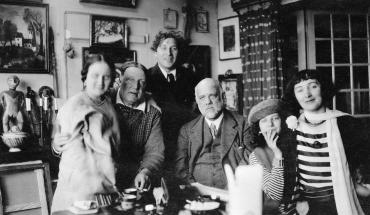 Photographie d'Ambroise Vollard et André Derain avec la famille Chagall, dans une pièce décorée de tableaux et sculptures.