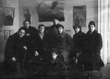 Group photograph with Chagall surrounded by warmly dressed young students, in front of several paintings.