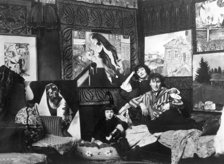 Marc et Bella Chagall, à côté de leur fille Ida, posent sur un divan de leur salon, derrière eux sont accrochés cinq tableaux.