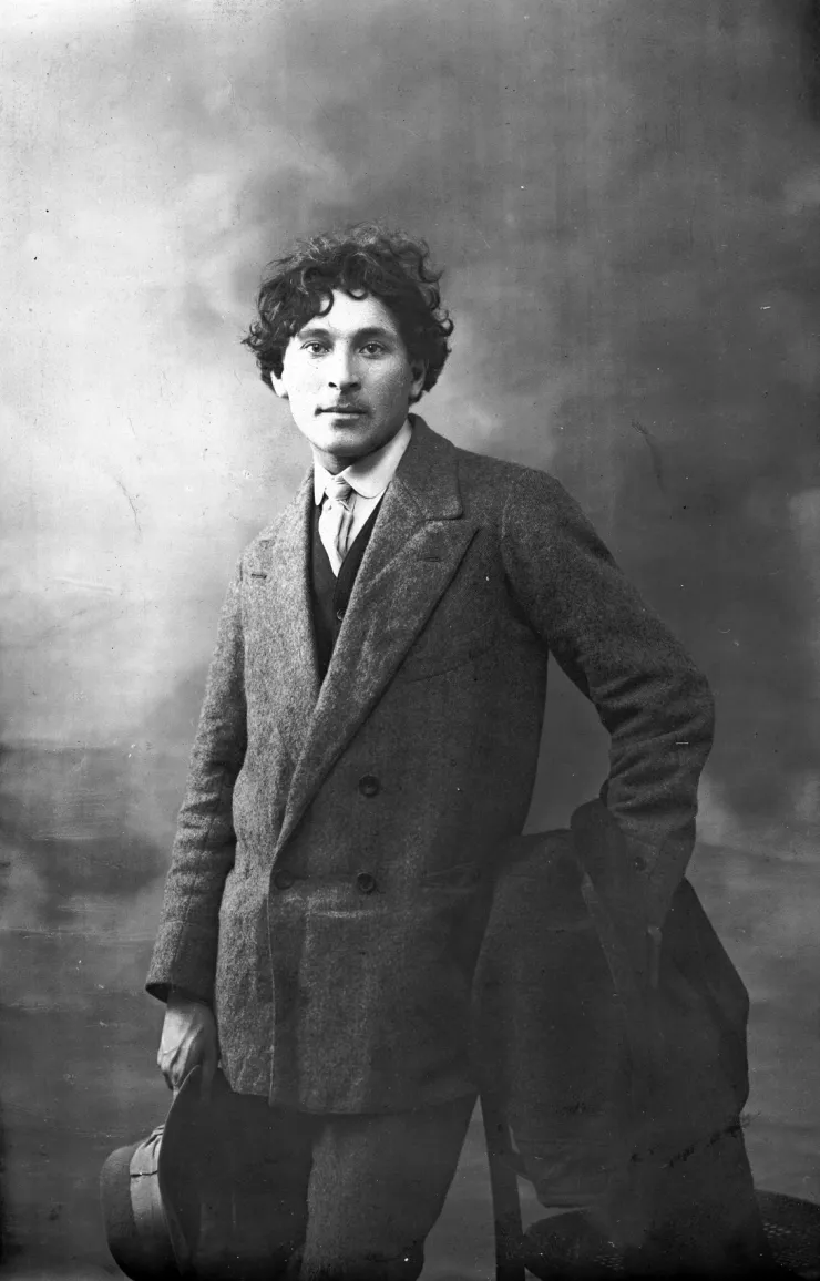 Marc Chagall, âgé d'une vingtaine d'années, pose en pardessus et chapeau à la main.